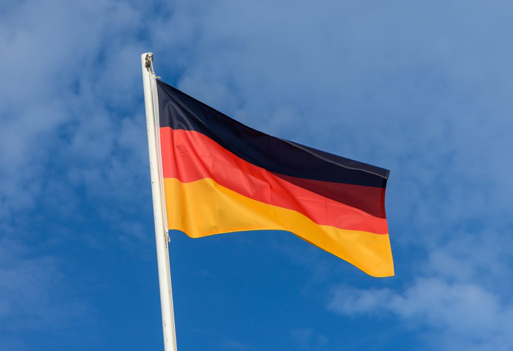 The German flag flutters proudly against a clear blue sky, showcasing its black, red, and yellow colors. This outdoor display captures a moment of national pride.